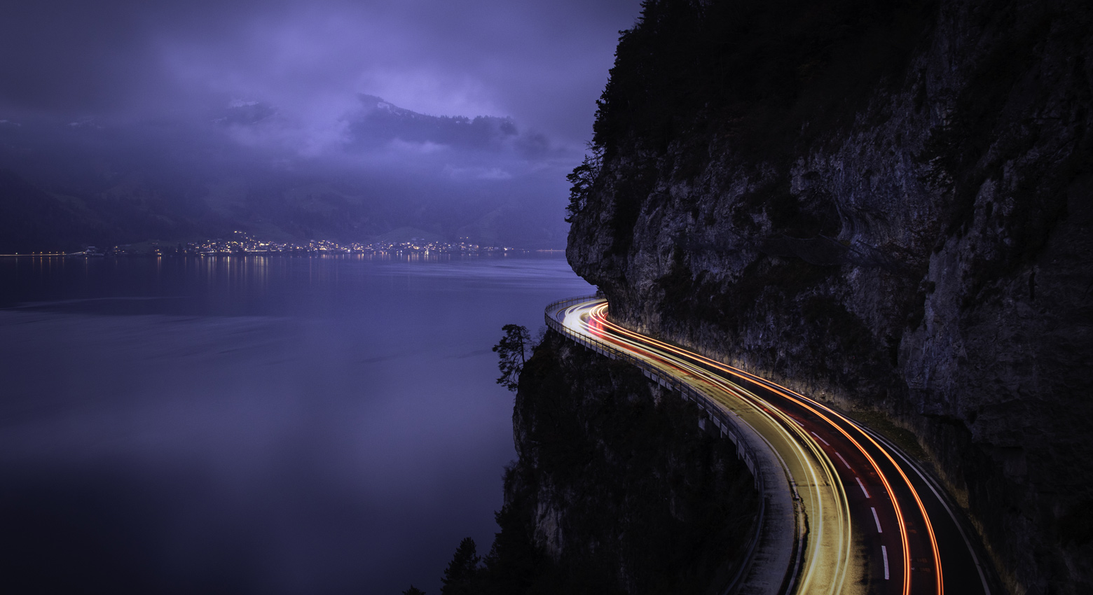 Cliff side at night with winding road and trailing lights 