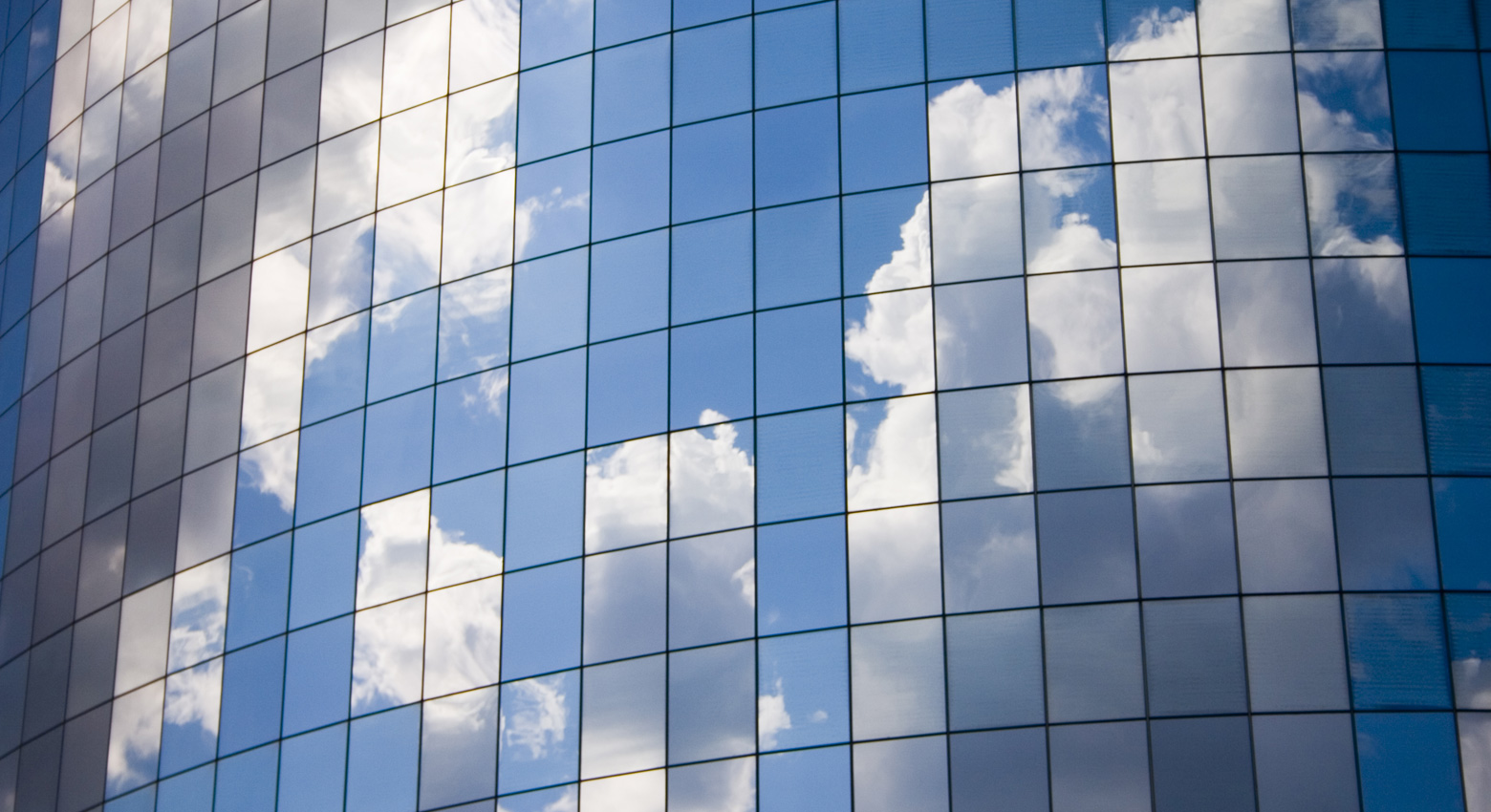 A bright blue sky and fluffy white clouds reflected in the curve of a New York skyscraper.